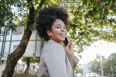 Happy businesswoman talking on mobile phone near tree - MDOF01508