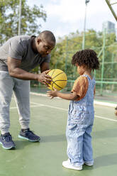 Vater schenkt seinem Sohn auf dem Sportplatz einen Basketball - IKF01236
