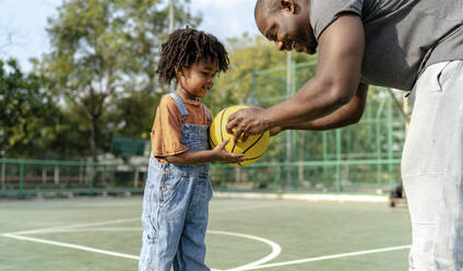 Lächelnder Vater gibt seinem Sohn auf dem Sportplatz einen Basketball - IKF01237