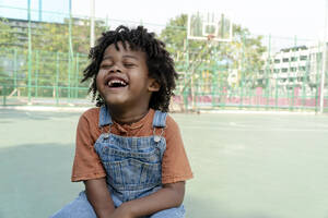 Junge mit lockigem Haar lachend auf Sportplatz - IKF01242