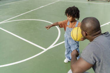 Vater mit Junge hält Basketball und gestikuliert auf Sportplatz - IKF01254