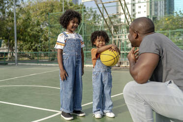 Smiling children talking to father on basketball court - IKF01255