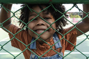 Lächelnder Junge schaut durch den Zaun - IKF01263