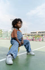 Cute boy sitting on basketball on sports court - IKF01266