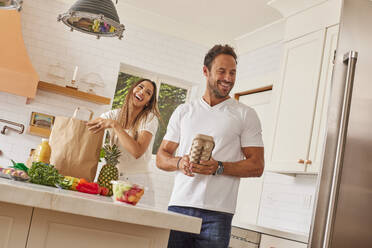 Smiling couple with paper shopping bag and groceries in kitchen - TETF02228