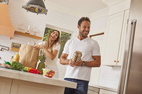 Lächelndes Paar mit Papiertüte und Lebensmitteln in der Küche - TETF02228