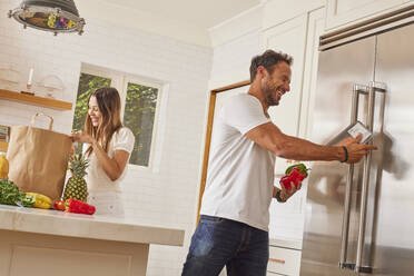 Lächelndes Paar mit Papiertüte und Lebensmitteln in der Küche - TETF02229