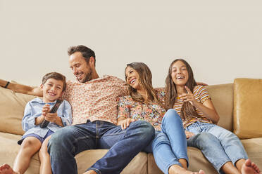 Lächelnde Familie mit zwei Kindern (8-9, 12-13), die auf dem Sofa fernsehen - TETF02232