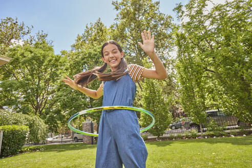 Smiling girl (12-13) playing with hula hoop in park - TETF02235