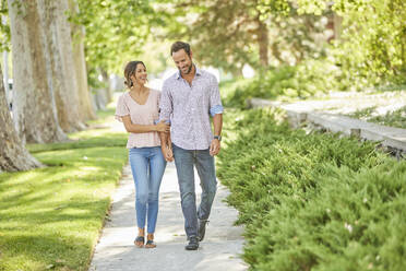 Smiling couple holding hands, walking on treelined sidewalk - TETF02238