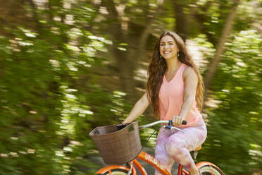 Smiling young woman riding bicycle in park - TETF02246