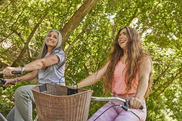 Mother and adult daughter riding bicycles in park - TETF02247