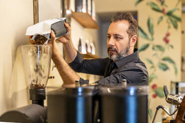 Barista legt Kaffeebohnen in die Kaffeemaschine - DLTSF03646