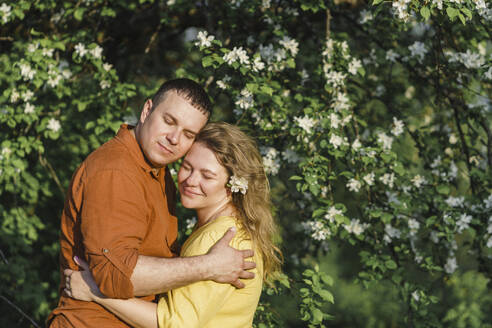 Glückliches Paar, das sich vor einem blühenden Baum umarmt - VBUF00389