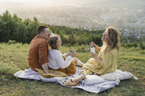 Happy family having tea on picnic blanket in meadow - VBUF00397