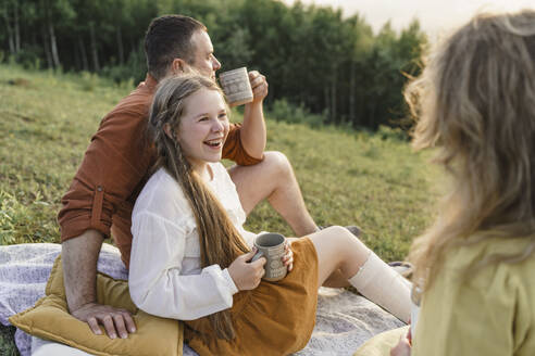 Smiling family having tea on picnic blanket in meadow - VBUF00398
