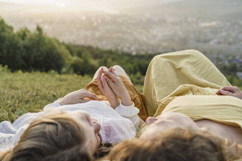 Mother and daughter holding hands and relaxing at sunset - VBUF00399