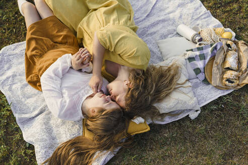 Mother and daughter rubbing noses and lying on picnic blanket - VBUF00400