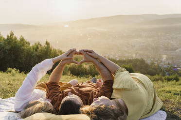Eltern mit Tochter gestikulierendem Herzzeichen bei Sonnenuntergang liegend - VBUF00402