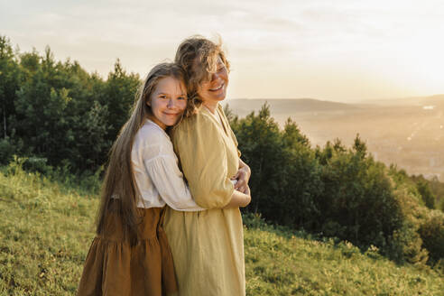 Smiling girl hugging mother at sunset - VBUF00406