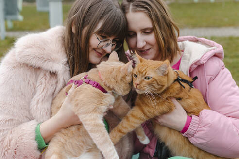 Lächelnde junge Frauen mit Katzen im Park - EHAF00108