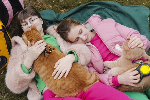Lächelnde junge Frauen liegen mit Katzen auf einer Decke - EHAF00109