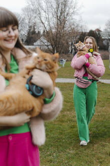 Zwei junge Frauen tragen Katzen und gehen im Park spazieren - EHAF00111