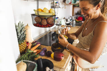 Smiling pregnant woman preparing oatmeal in kitchen - PCLF00720