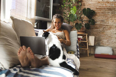 Lächelnde schwangere Frau mit Laptop und Katze auf dem Sofa zu Hause - PCLF00732