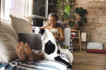 Smiling pregnant woman with laptop and cat sitting on sofa at home - PCLF00732