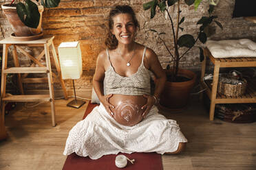 Lächelnde schwangere Frau, die zu Hause Feuchtigkeitscreme auf den Bauch aufträgt - PCLF00740