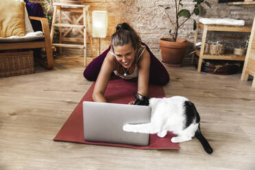 Smiling woman using laptop and playing with cat at home - PCLF00742