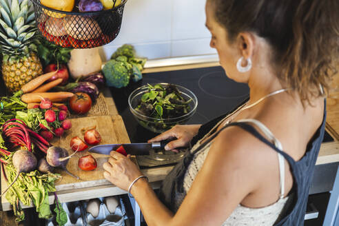 Schwangere Frau schneidet Tomaten in der Nähe verschiedener Gemüse in der Küche zu Hause - PCLF00746
