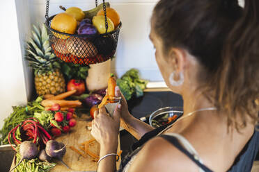 Frau schält Karotte in der Küche zu Hause - PCLF00748