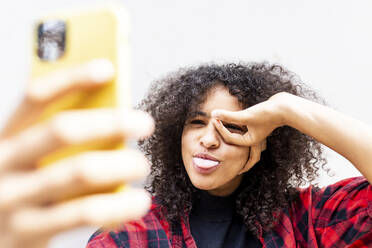 Happy woman gesturing and taking selfie with smart phone in front of wall - WPEF07706