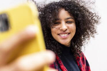 Happy woman taking selfie with mobile phone in front of wall - WPEF07708