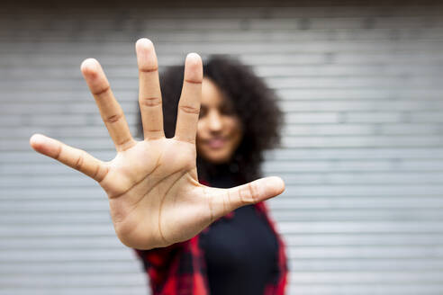 Woman showing stop sign gesture in front of shutter - WPEF07716