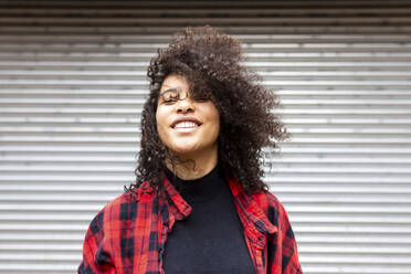 Smiling woman with curly hair in front of shutter - WPEF07719