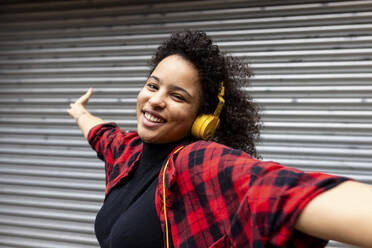 Smiling woman listening to music through headphones in front of shutter - WPEF07722