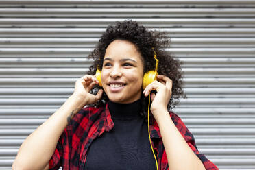 Happy woman listening to music through headphones in front of shutter - WPEF07723