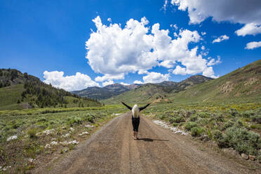 USA, Idaho, Sun Valley, Rear view of senior woman standing with arms raised on road and looking at mountains - TETF02283