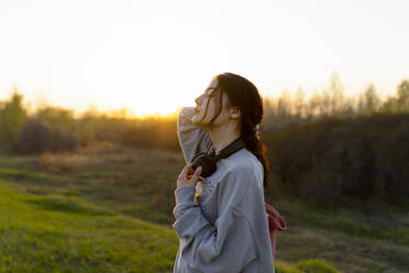 Porträt einer jungen Frau mit Kopfhörern auf einer Wiese bei Sonnenuntergang - TETF02291