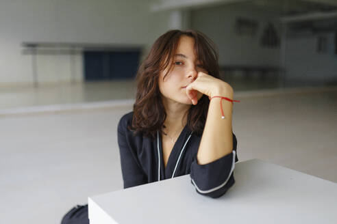 Portrait of young woman looking at camera while sitting in dance studio - TETF02294