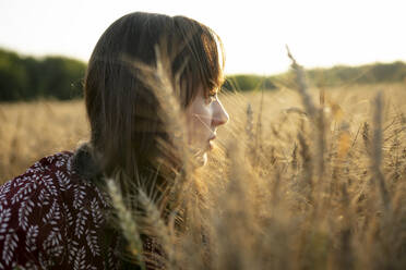 Porträt einer jungen Frau mit Blick auf ein landwirtschaftliches Feld bei Sonnenuntergang - TETF02305