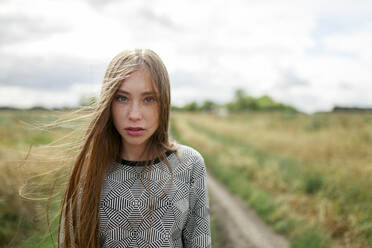 Porträt einer jungen blonden Frau, die in einem Feld in die Kamera schaut - TETF02314