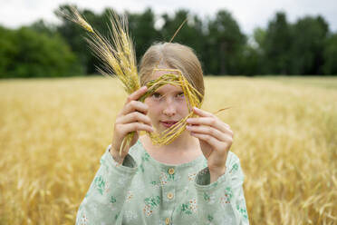 Junge Frau hält einen kleinen Weizenkranz auf einem Feld - TETF02319