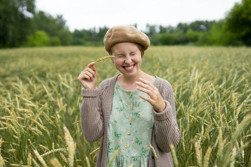 Smiling woman with closed eyes touching face with ear of wheat - TETF02320