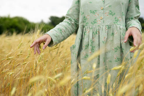 Junge Frau berührt Weizenähren auf einem Feld - TETF02321