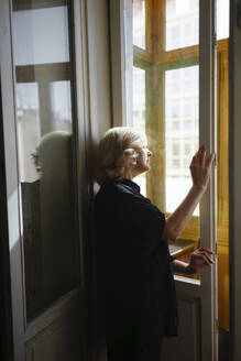 Frau steht am Fenster und schaut nach draußen - TETF02332