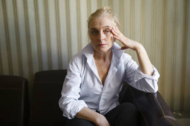 Ernste blonde Frau sitzt auf dem Sofa im Wohnzimmer - TETF02333
